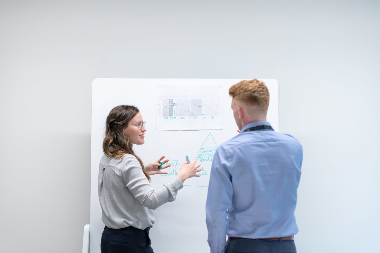 creative Two professionals discussing project plans at whiteboard in office setting.