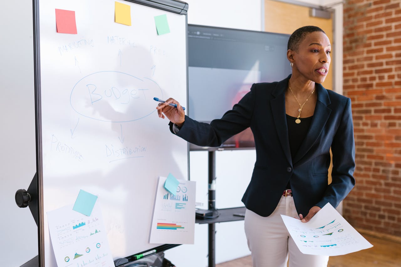 our-story Professional businesswoman explaining budget strategy on a whiteboard during a meeting.